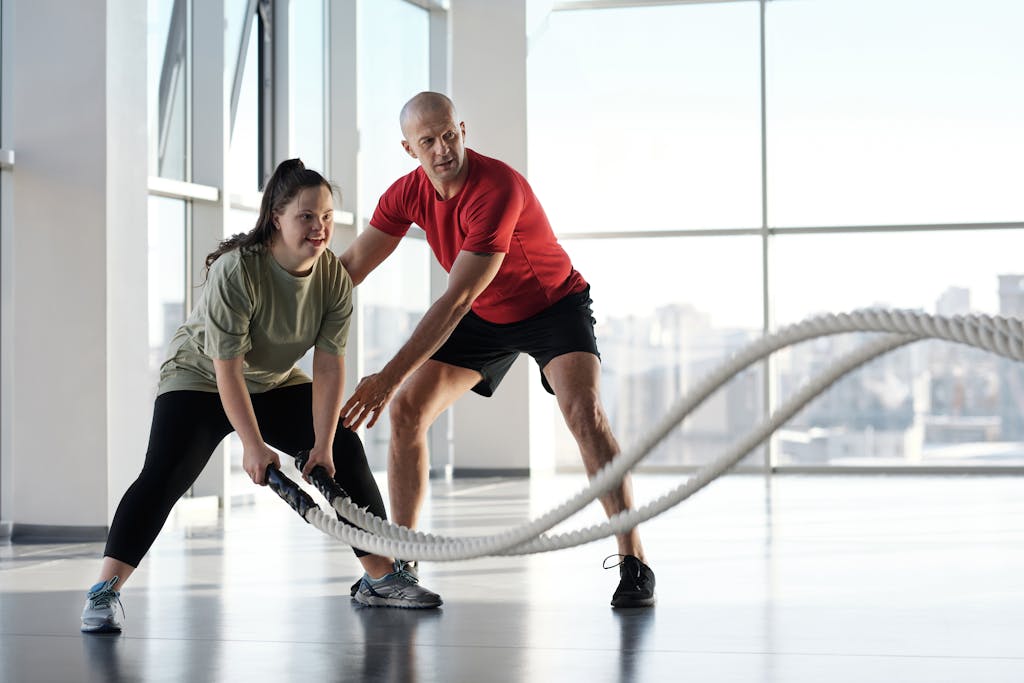 Woman and trainer engaging in rope workout in a bright gym, showcasing inclusivity and fitness motivation.